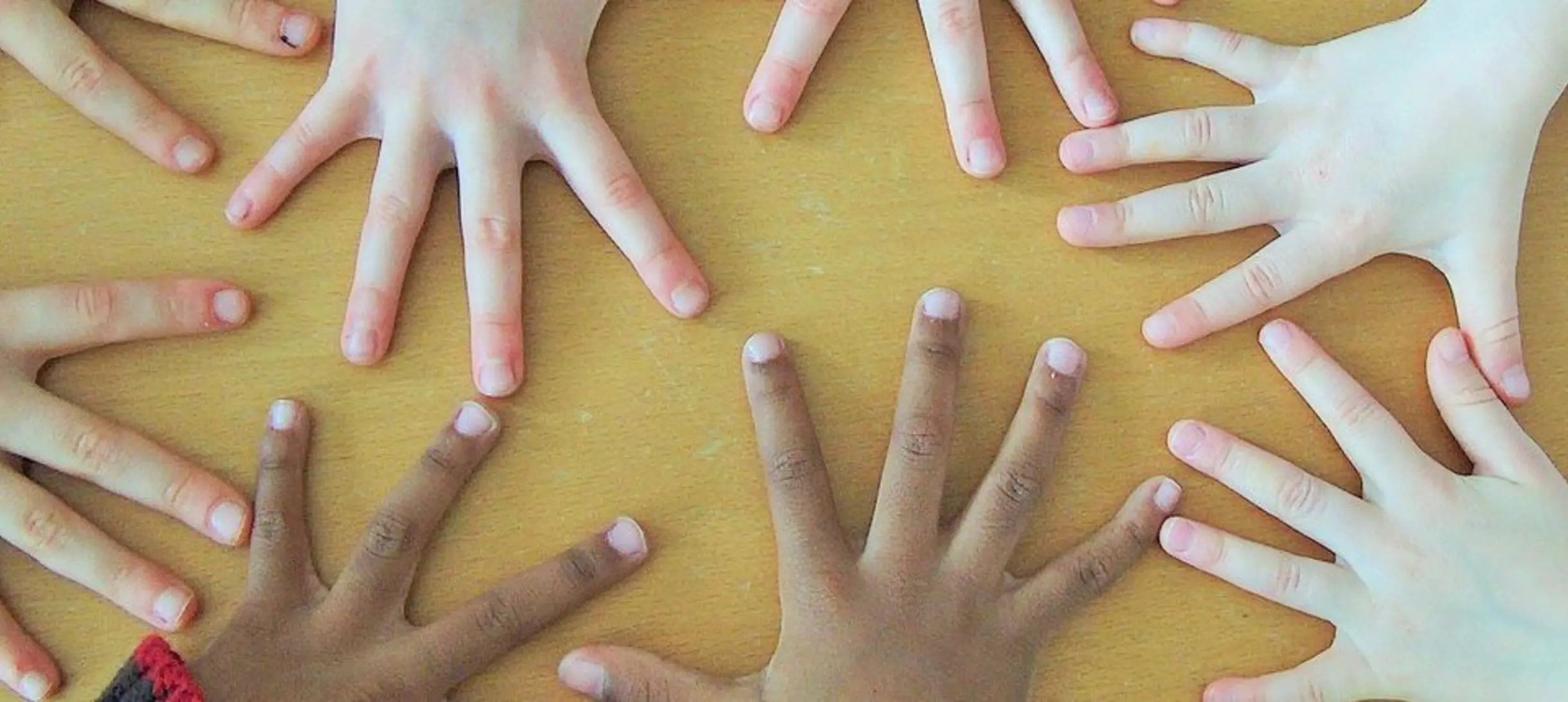 several pairs of hands with fingers outstretched covering a yellow surface