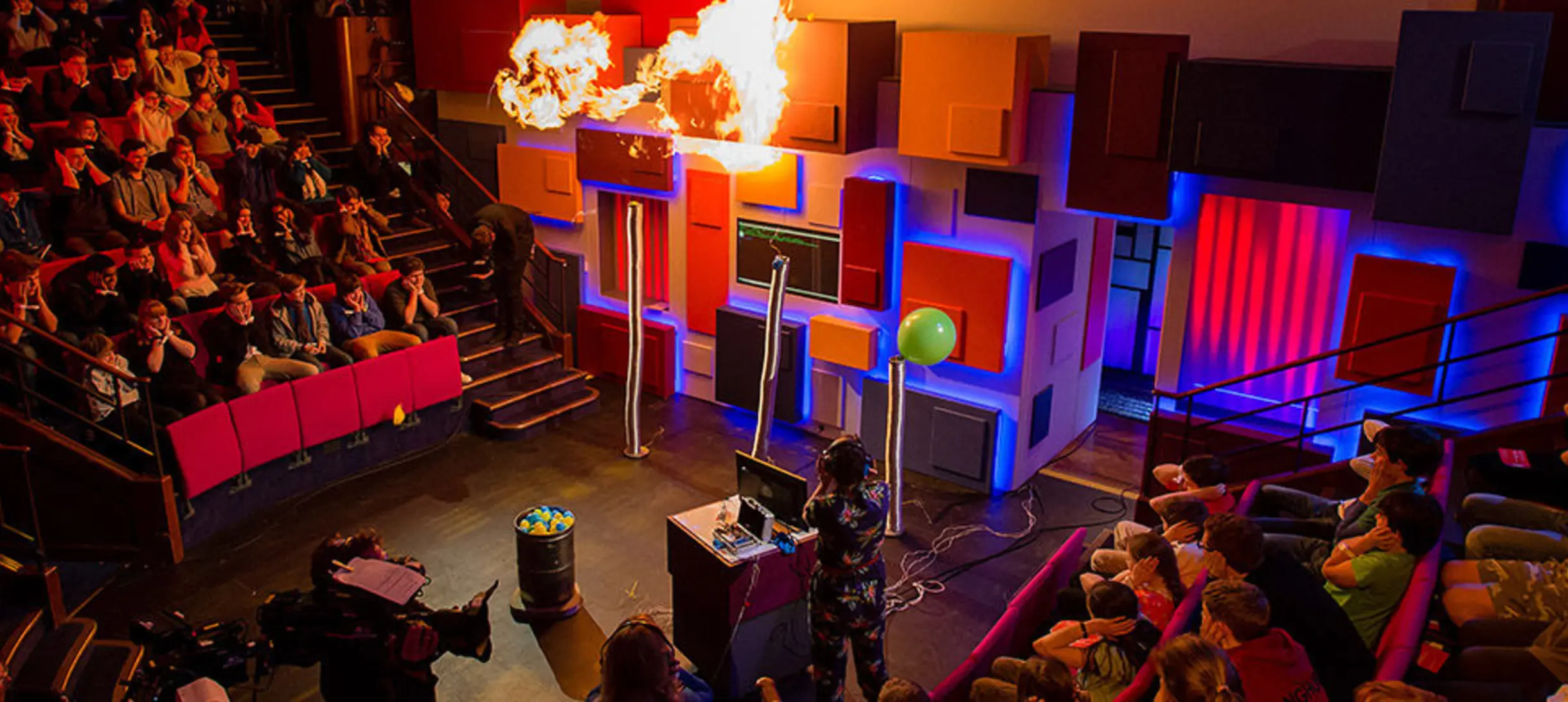 Christmas Lectures set with flames above it and an audience with hands  over their ears