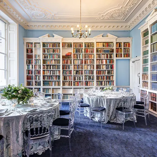 two round tables with chairs around them are in the middle of a large room with bookshelves lining the walls