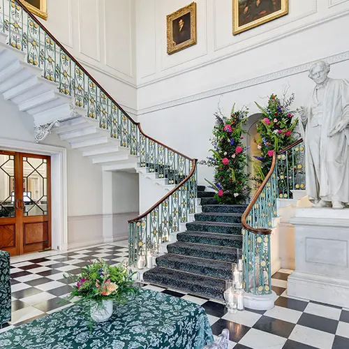 a grand staircase with soft carpets over a checkered floor and marble steps, there's also a statue of Michael Faraday