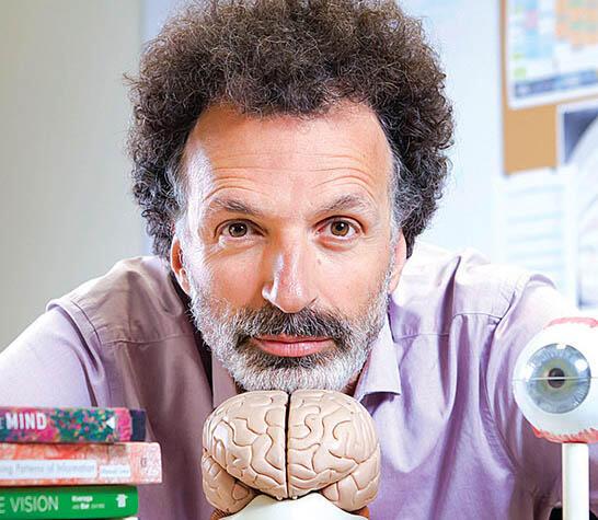 man with curly hair and a beard resting his chin on a small model of a brain