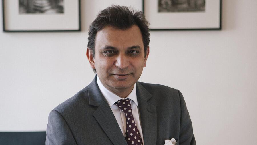 Porfile of Prokar Dasgupta, wearing a dark suit and against a light background.