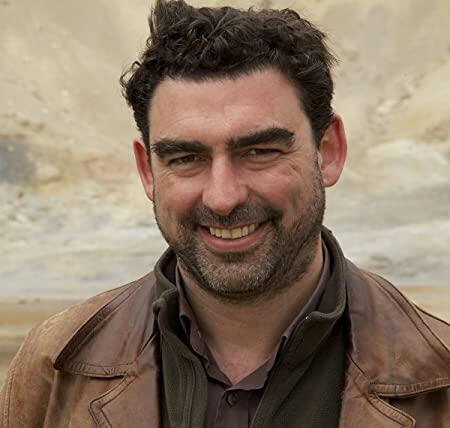 A profile of a man wearing a brown jacket and red shirt.