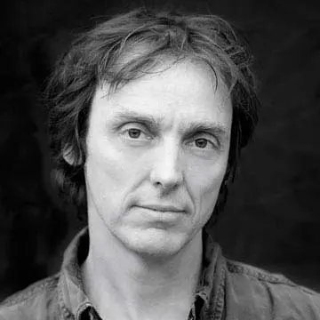 A black and white images of a man looking down the camera.