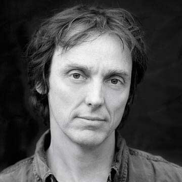 A black and white images of a man looking down the camera.