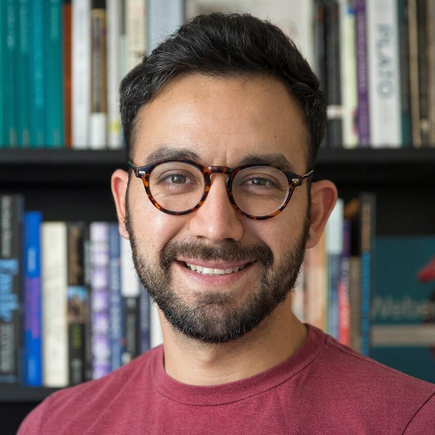 David is looking at the screen, wearing dark rimmed glasses and a red T-shirt. He is smiling.