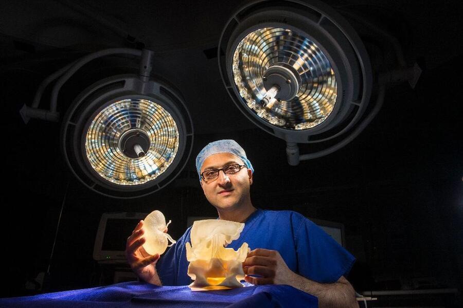 A surgeon is looking at the camera while holding artificial organs. There are bright lights behind him.