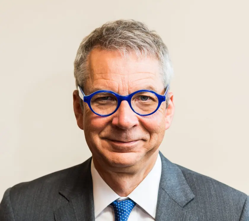 A man with black glasses is smiling towards the screen.