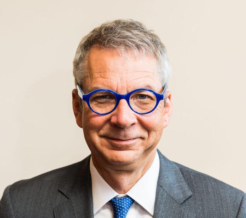 A man with black glasses is smiling towards the screen.