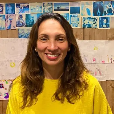 A woman is looking at the screen smiling. She is wearing a bright yellow top.