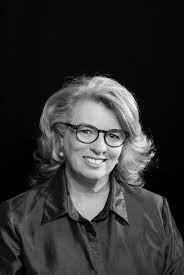 Alison is wearing glasses and looking at the camera. She is smiling.