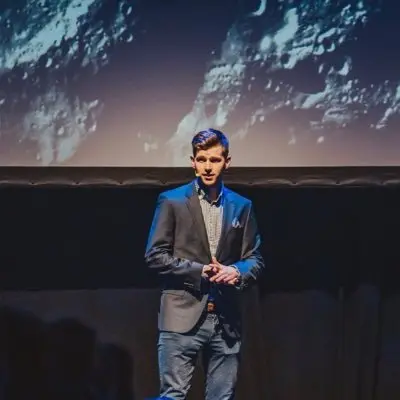 Calum is standing infront of a big screen showing space.