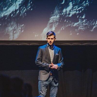 Calum is standing infront of a big screen showing space.