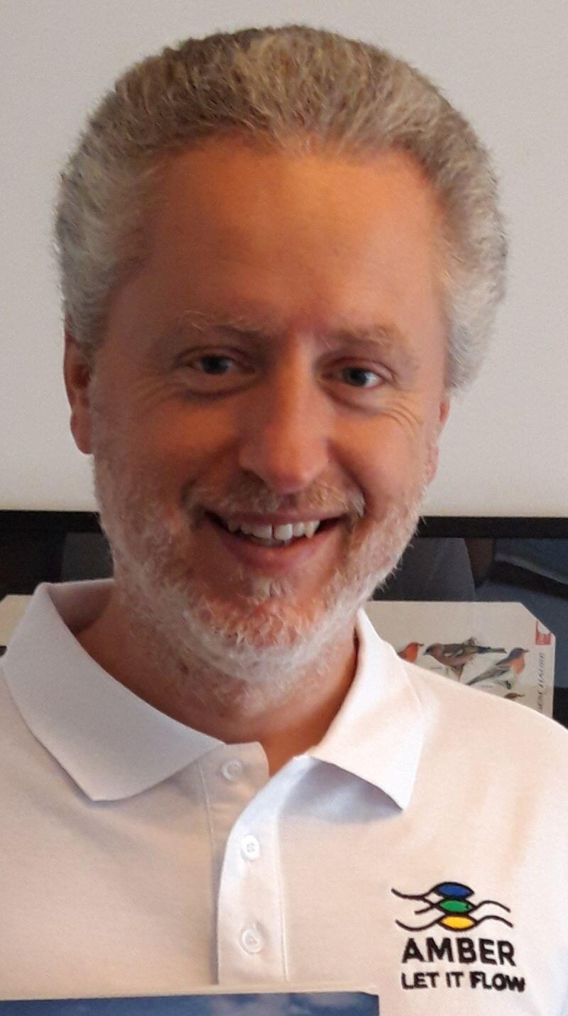A man with short grey hair is looking at the camera and smiling.