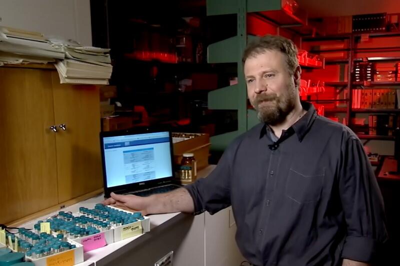 A man is standing in front of lots of specimens in small containers.