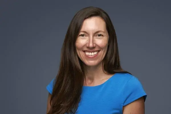 A picture of a woman smiling at the camera. She has long brown hair.