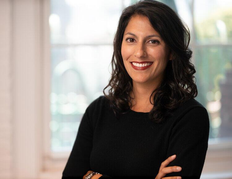 A woman with long dark hair is smiling towards the camera.