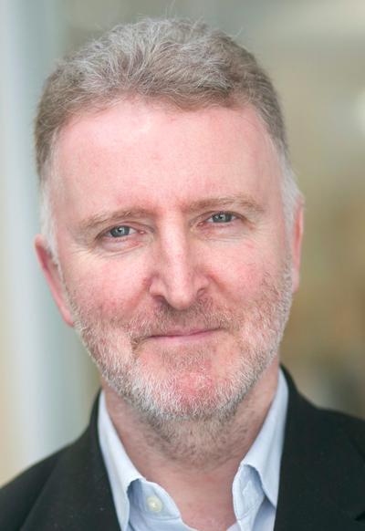 A man with short grey hair is smiling towards the camera.