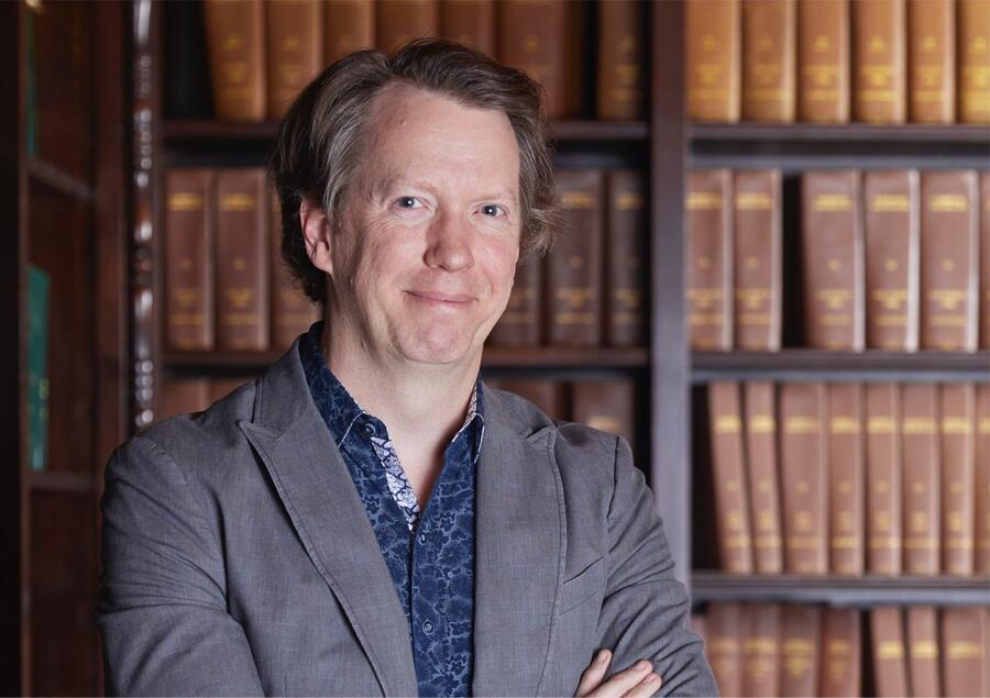 Sean is standing in front of a bookcase full of books.