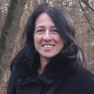 A woman is smiling at the camera. She has long brown hair.