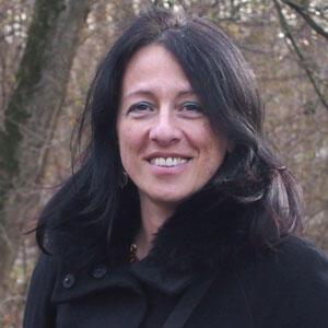 A woman is smiling at the camera. She has long brown hair.