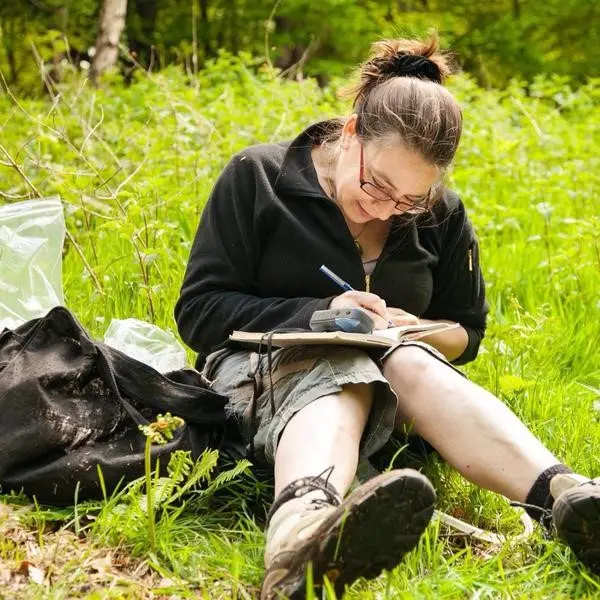 Erica sat on the floor writing on a clipboard in a field