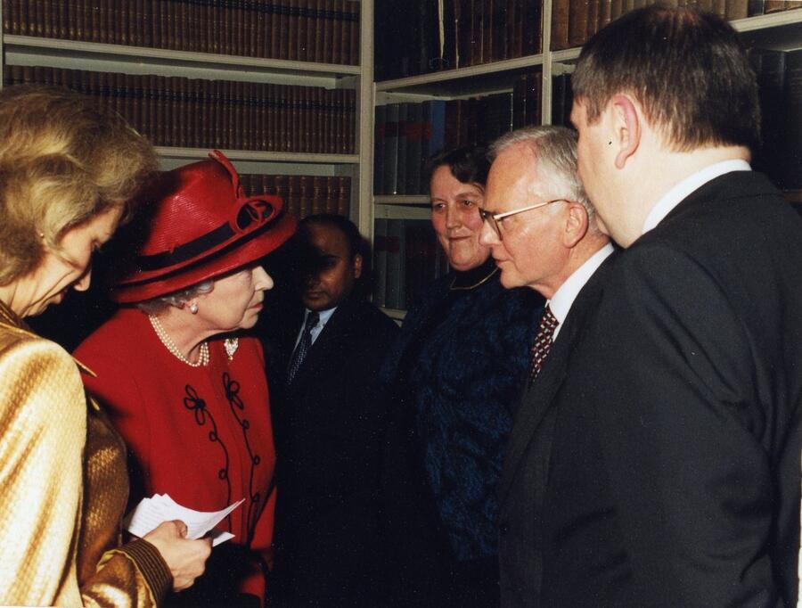 The Queen wearing a red dress and hat talking to a group of men in suits