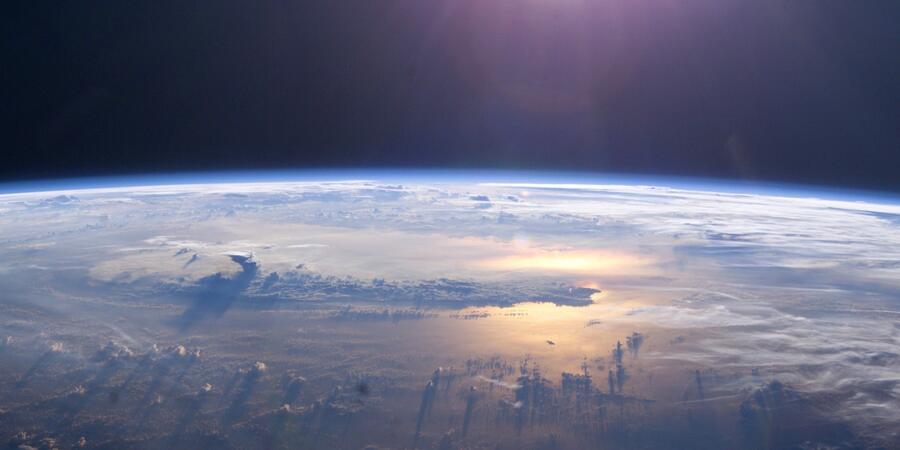A photo of the Earth seen from orbit, showing the curvature of the planet, fluffy clouds and the sun shining on the ocean