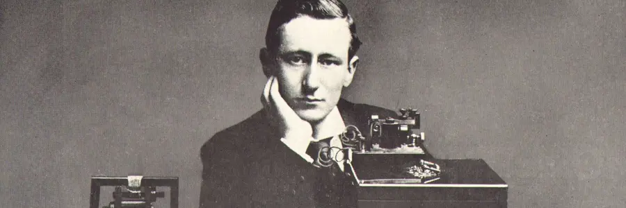 A young Marconi sitting at a table behind his equipment