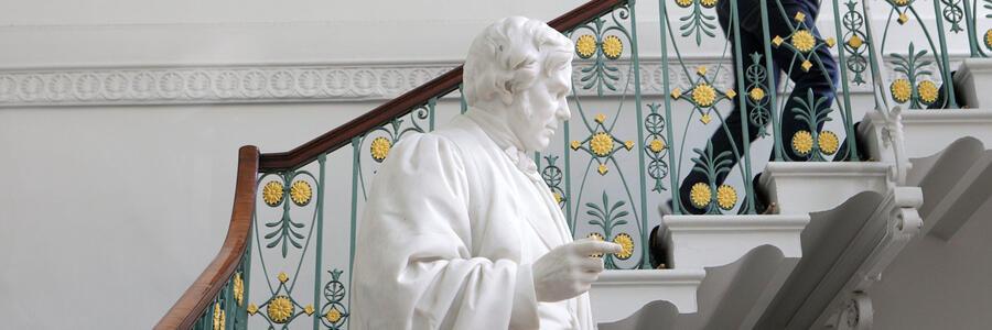 The Faraday statue in the grand entrance of the Ri. We can see a person climbing the stairs next to it