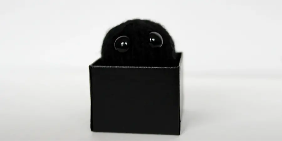 A teeny tiny crochet black hole in the shape of a ball with big round eyes