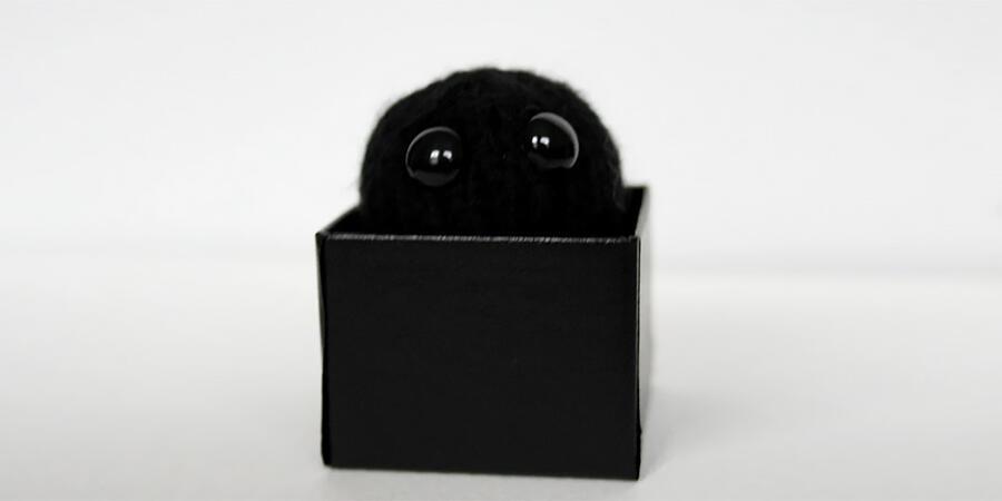 A teeny tiny crochet black hole in the shape of a ball with big round eyes