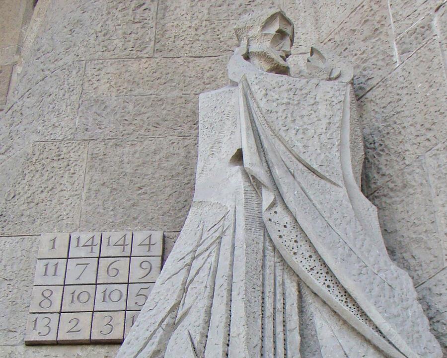A stone magic square on the side of the Sagrada Familia, next to a statue of two people kissing