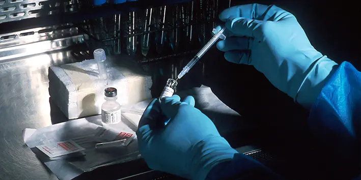 A person wearing blue gloves handling a vial and a syringe
