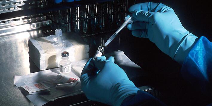 A person wearing blue gloves handling a vial and a syringe