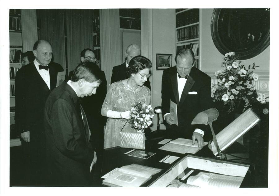 Black and white photograph of Queen Elizabeth holding a bouquet and looking at a handwritten book