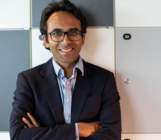 Ravi Gupta with his arms crossed, wearing a dark jacket and light shirt, smiling