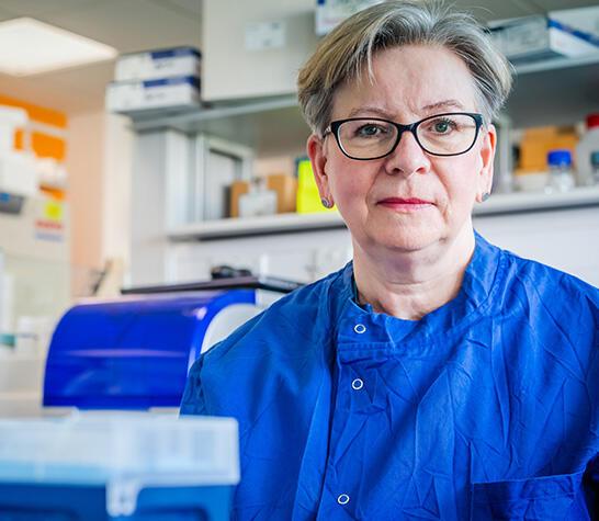Sharon Peacock in a dark blue lab coat sitting behind a scientific apparatus