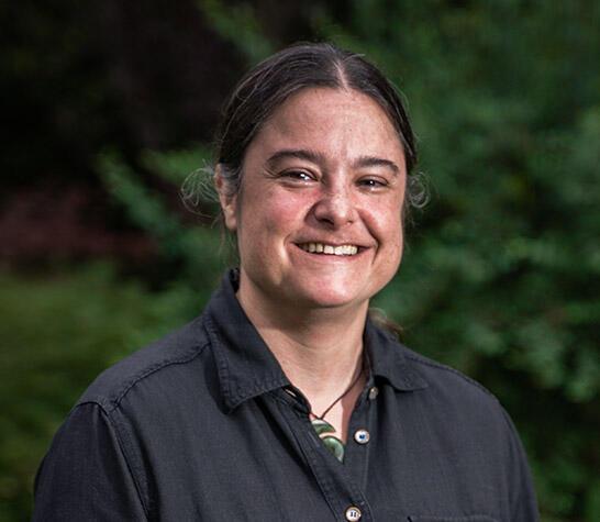 a woman with her dark hair tied back and wearing a black button up shirt and a jade spiral necklace