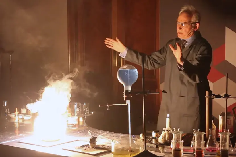 a man in lab coat holding his hands away from an explosive deomonstration