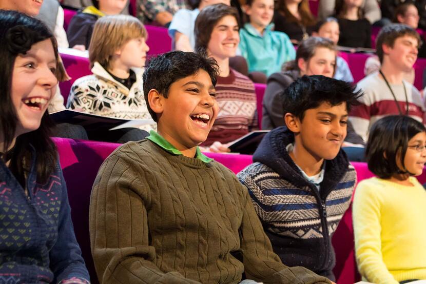 children in an audience smiling and cheering at something we cannot see