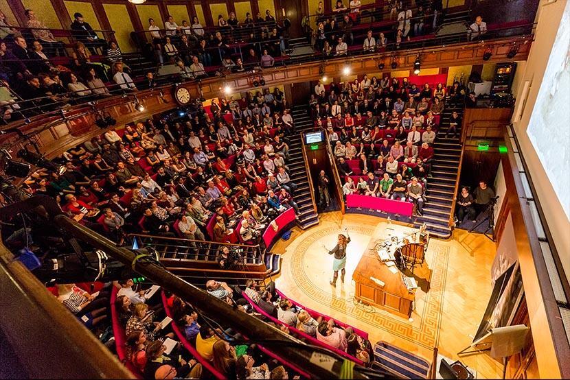 the Ri lecture theatre view from high up, all the chairs are taken and a person is talk to the crowd