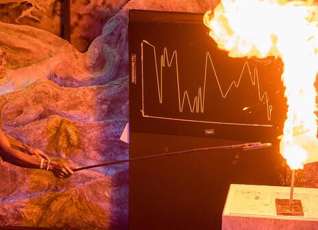 Chris Jackson holding a long stick with a match at the end setting fire to an experiment