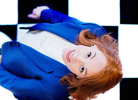 Hannah Fry in a blue suit looking up, standing in a chequered floor
