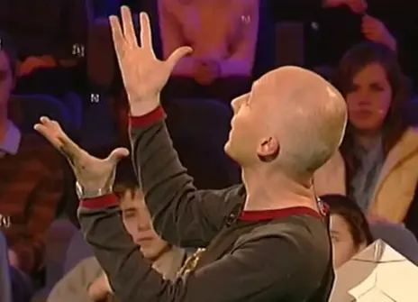 Marcus du Sautoy turned to the side with his hands in the air in the Ri Theatre
