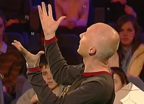 Marcus du Sautoy turned to the side with his hands in the air in the Ri Theatre