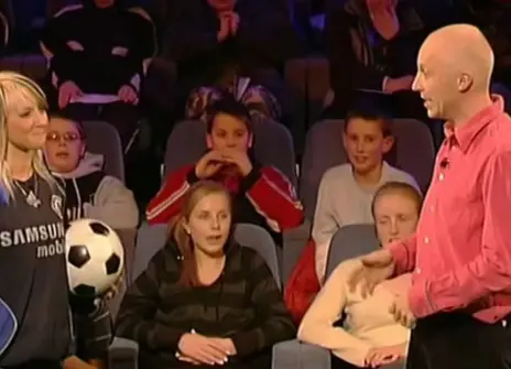 Marcus du Sautoy standing with a teenage girl who is holding a football, in front of an audience 