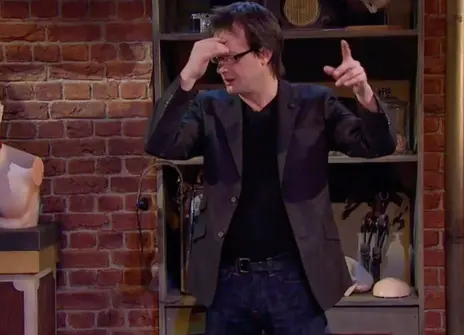 Bruce Hood with one hand on his head, standing in front of a bookcase 