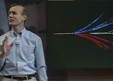 Frank Close speaking in front of a graphic of different coloured lines, in the Ri Theatre