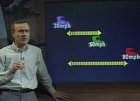 Frank Close speaking in front of a graphic of three cars with different speed limits listed next to them 